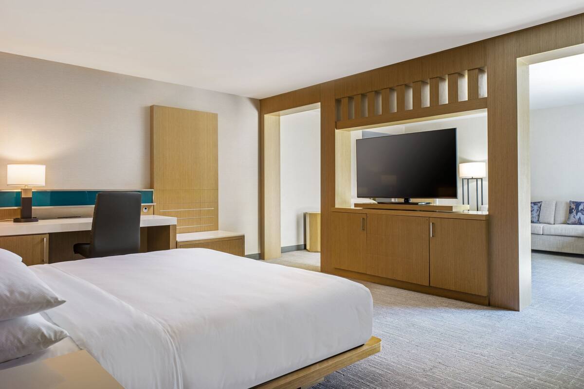 A hotel room with a bed, a desk with a chair, a television, and a sofa.