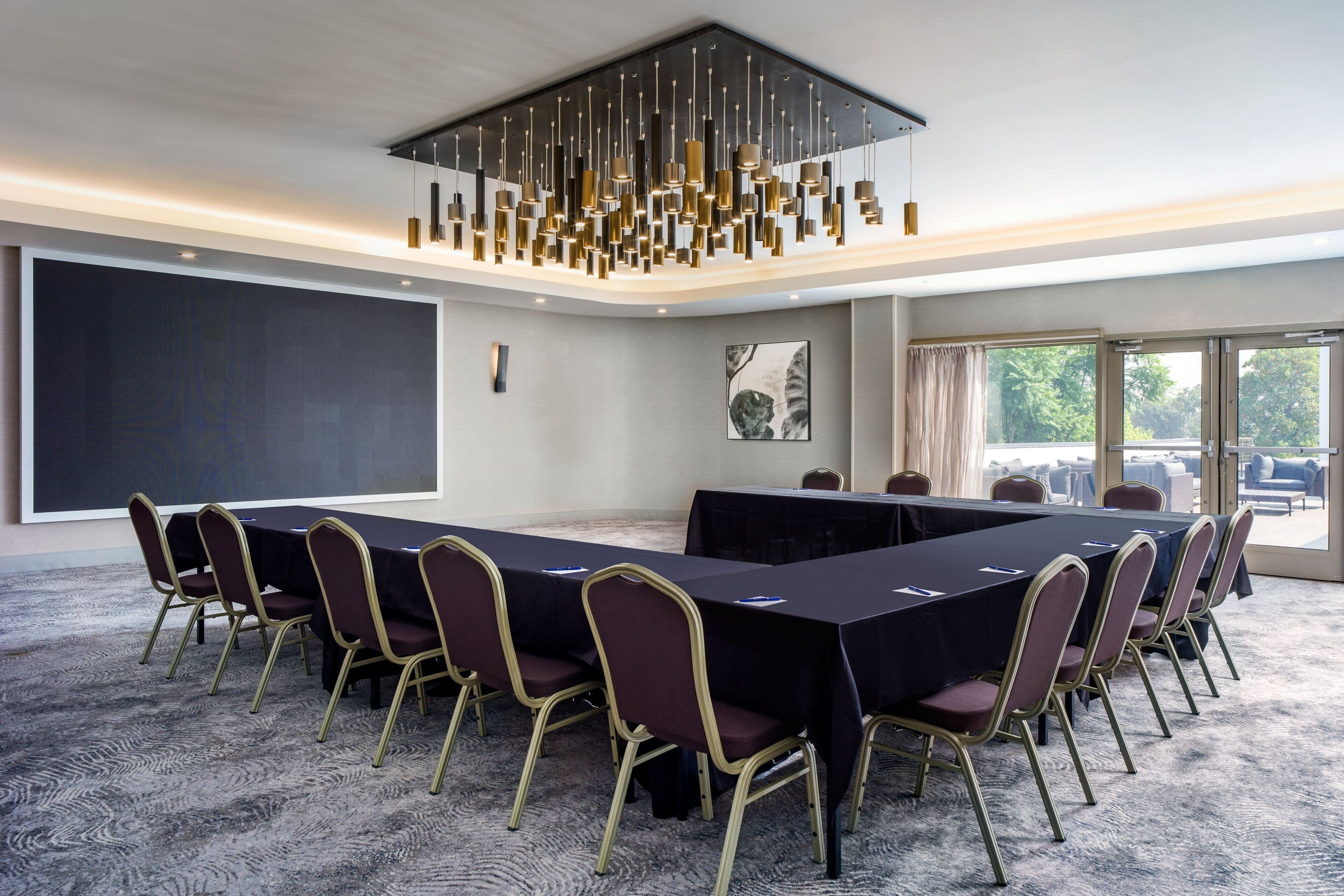 Un salón de conferencias con una larga mesa, sillas y una lámpara de araña moderna.