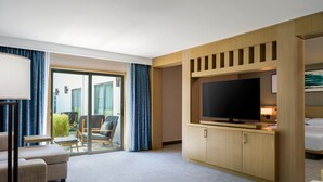 A hotel room with a large flat-screen TV, a sofa, a small table, and a balcony with chairs and a plant. - Delta Hotels by Marriott Ontario Airport (Ontario)