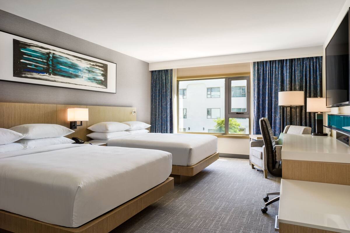 A hotel room with two beds, a desk, a chair, a TV, and a window with curtains.