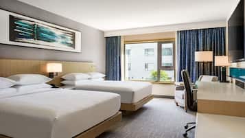 Habitación de hotel con dos camas, un escritorio, una silla, un televisor y una ventana con cortinas.