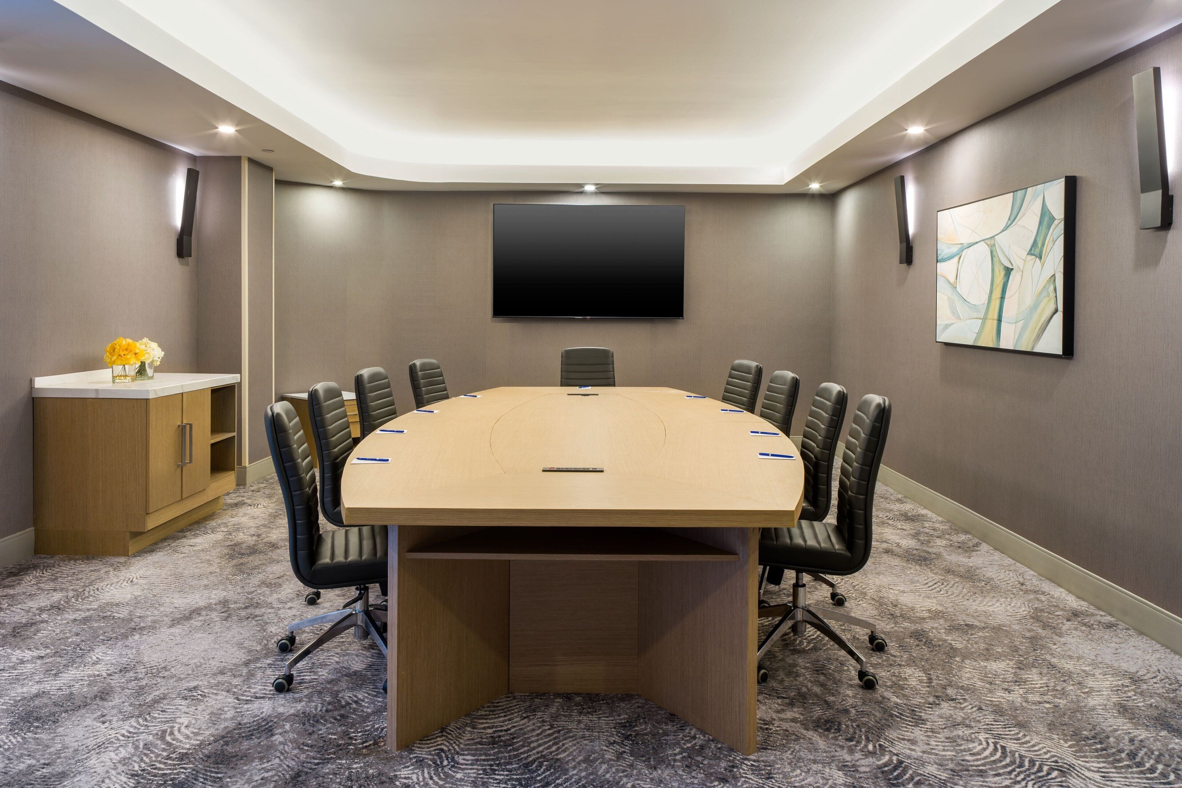 Un salón de conferencias con una mesa grande, sillas, un televisor y un armario.