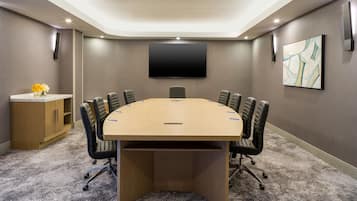Un salón de conferencias con una mesa grande, sillas, un televisor y un armario.