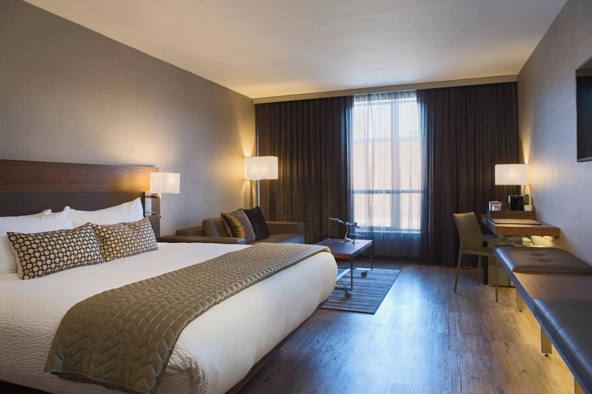 A hotel room with a large bed, a desk, a chair, and a sofa.