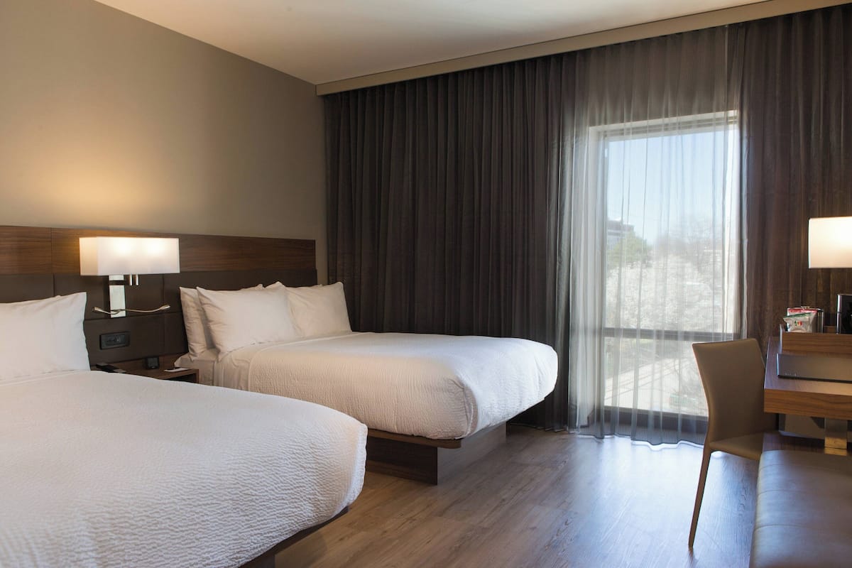 A hotel room with two beds, a desk, and a chair.
