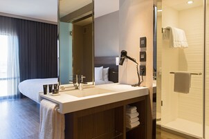 Un baño de hotel moderno con un espejo grande, lavamanos dobles, secador de pelo y cabina de ducha con paredes de vidrio.