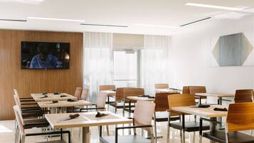 A modern conference room with multiple tables and chairs, a large flat-screen TV on the wall, and a geometric art piece on the wall.