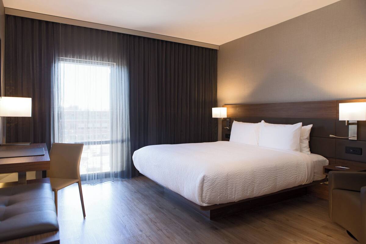 A hotel room with a large bed, a desk, a chair, and a window with curtains.