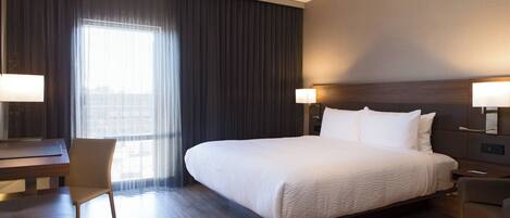 A hotel room with a large bed, a desk, a chair, and a window with curtains.