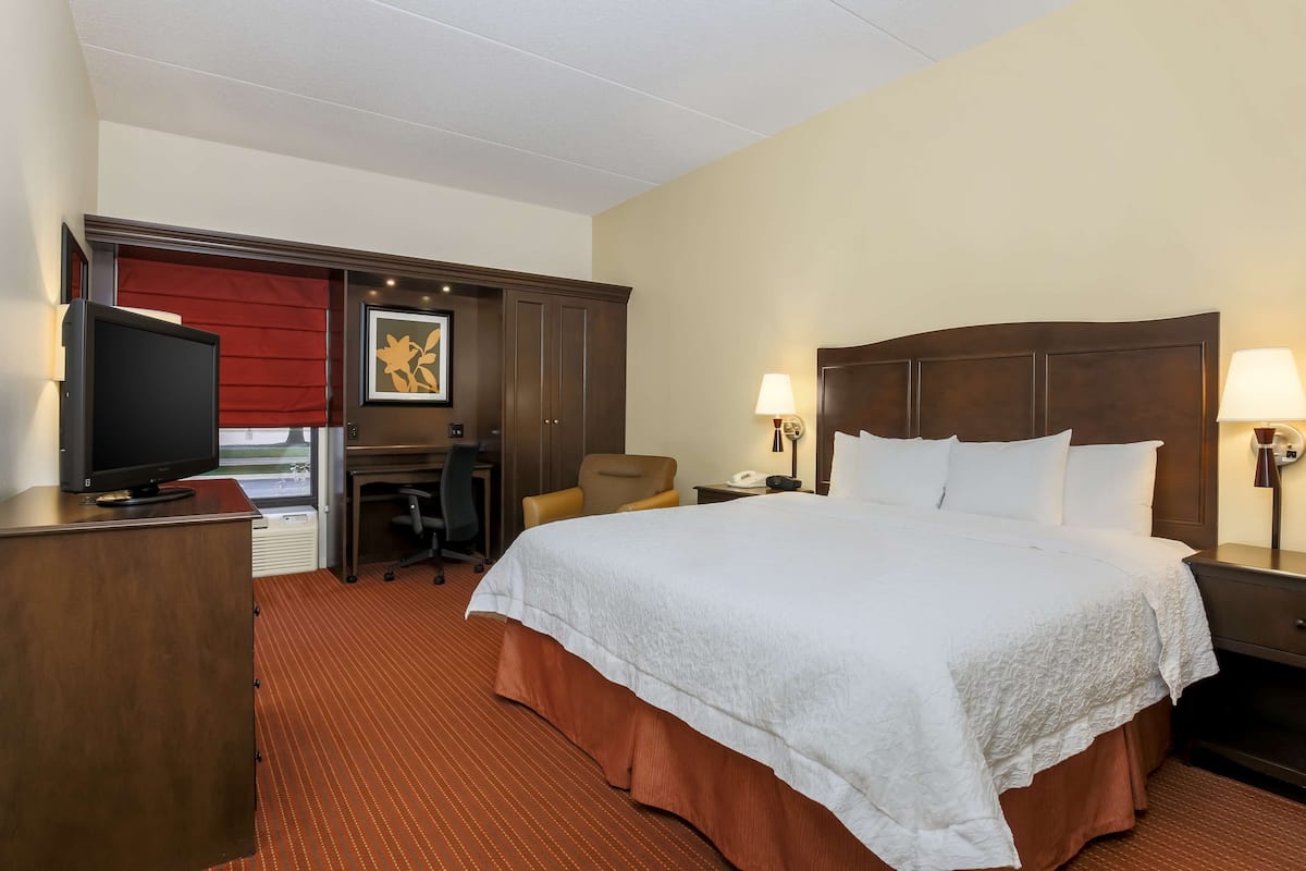 A hotel room with a large bed, a desk with a computer, a television, and two bedside lamps.