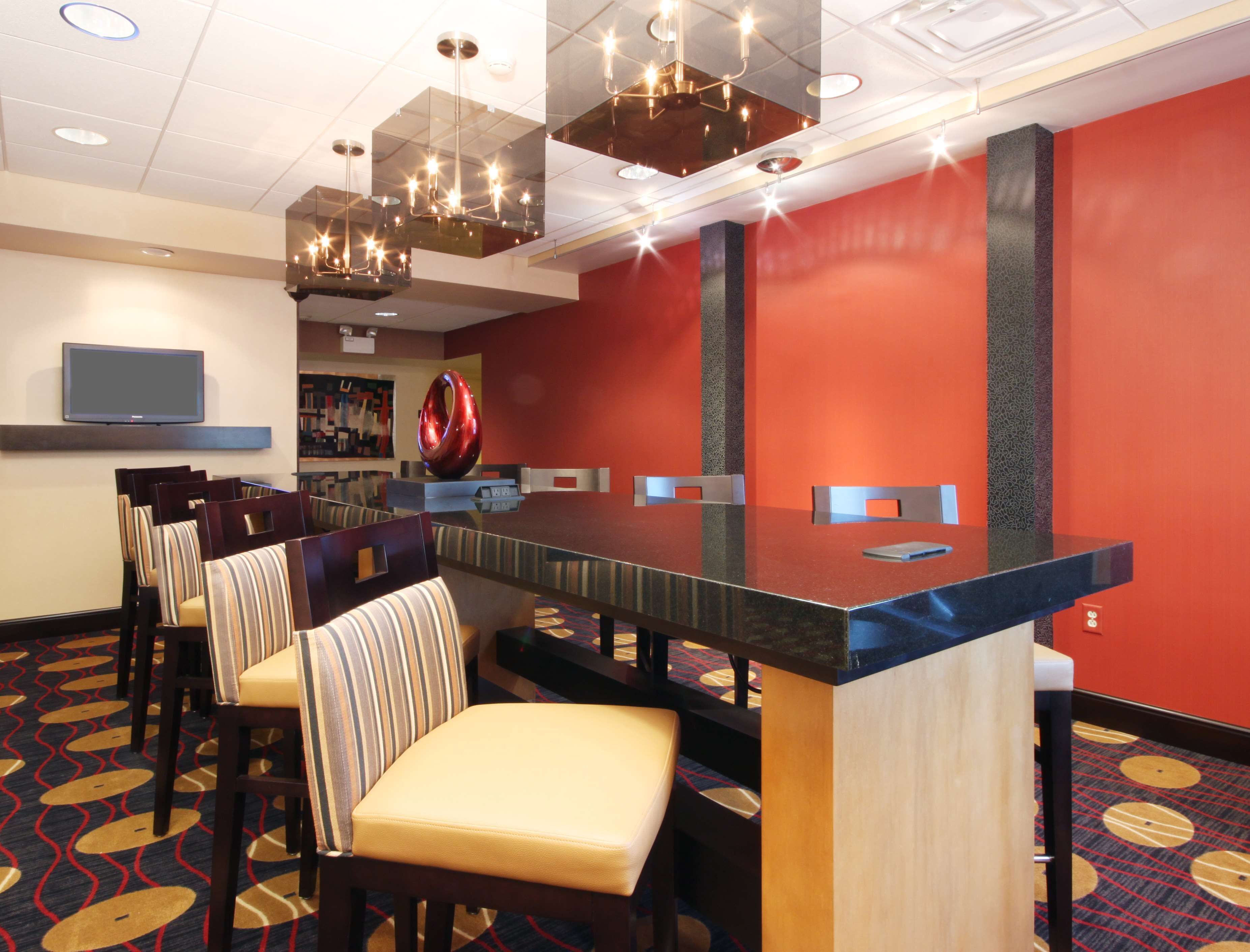A conference room with a long table, chairs, a TV, and a red accent wall.