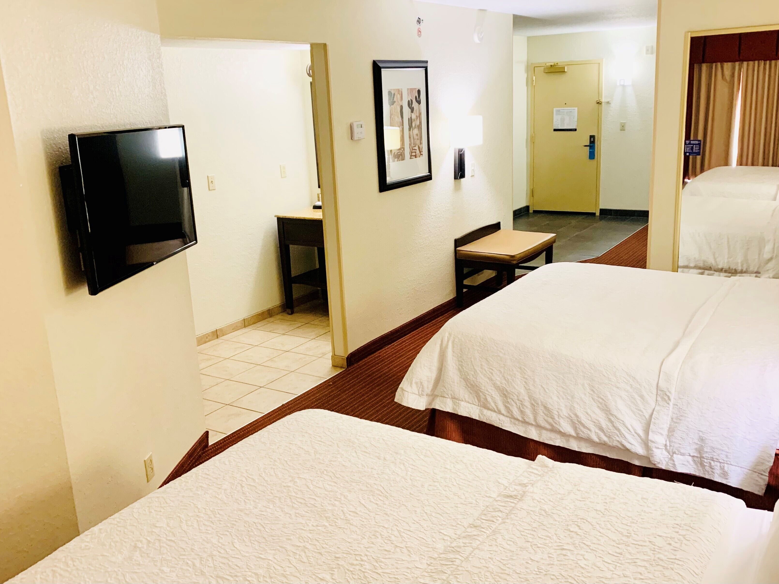 A hotel room with two beds, a television, a desk, and a chair.