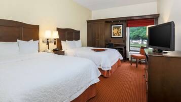 Quarto de hotel com duas camas, uma escrivaninha com televisão e uma janela com veneziana vermelha.