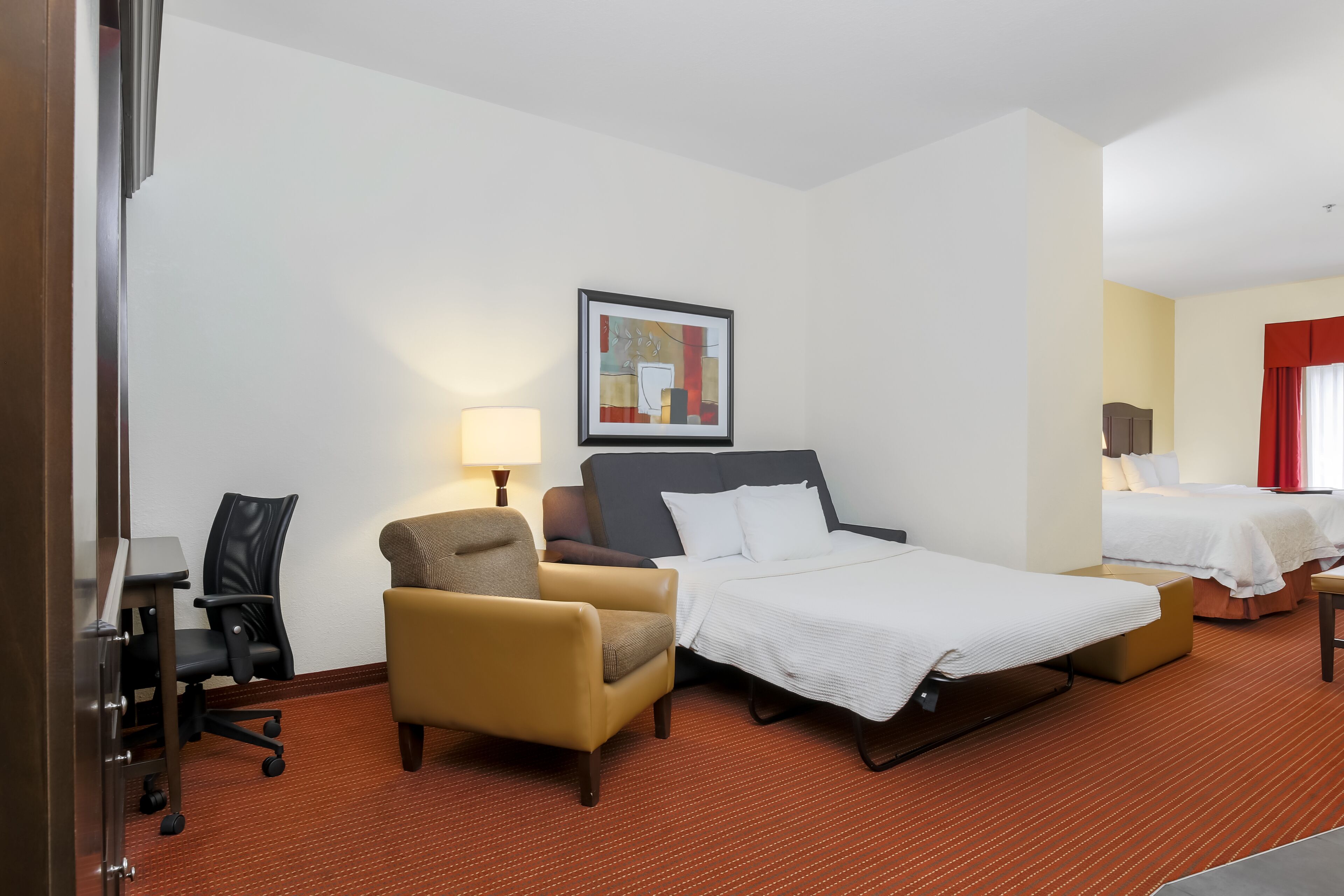 Une chambre d’hôtel avec un lit, une chaise, un bureau, une lampe et un tableau au mur.