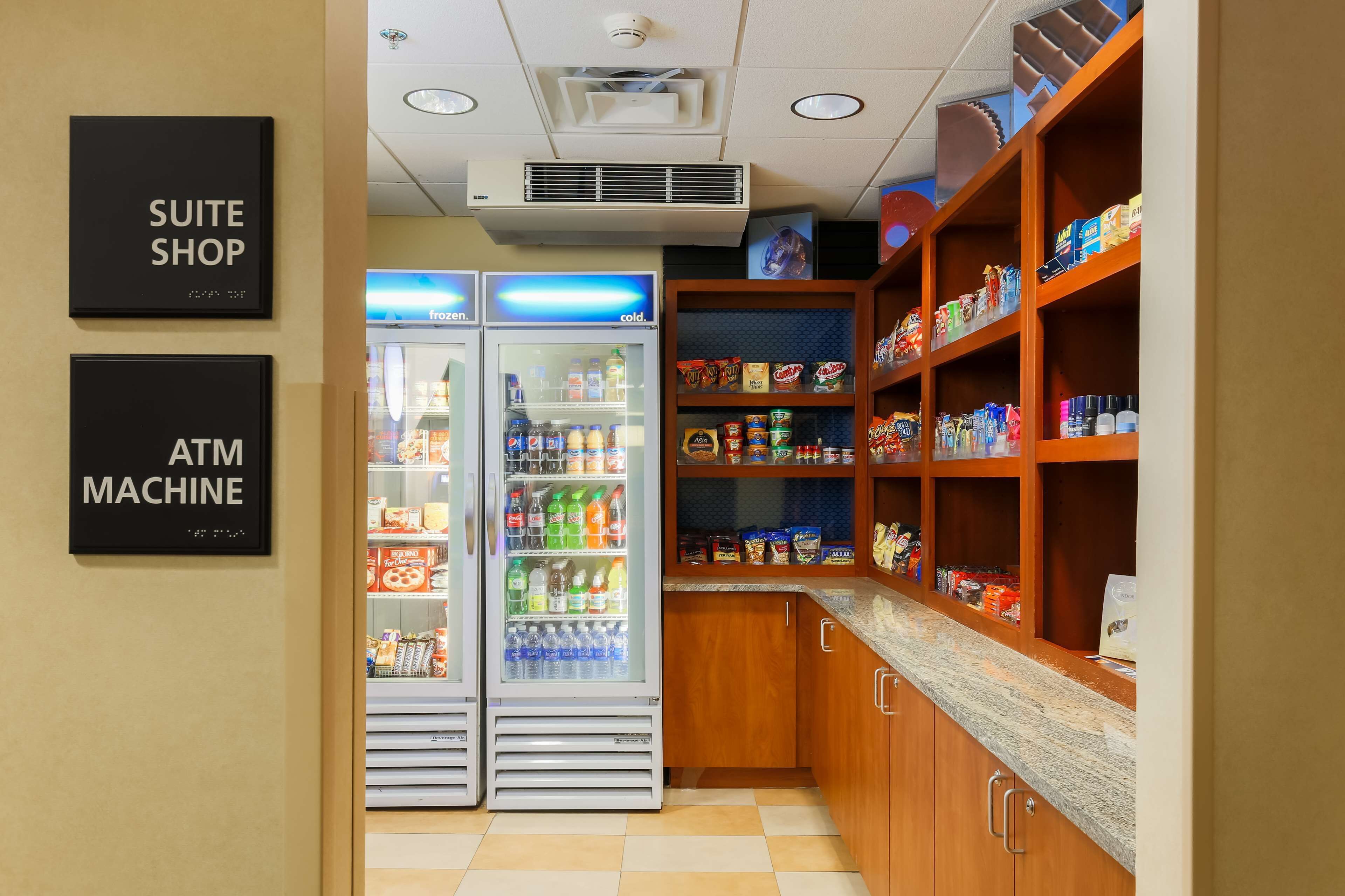 A kitchenette with a refrigerator, freezer, and shelves stocked with snacks and beverages.