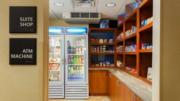 A kitchenette with a refrigerator, freezer, and shelves stocked with snacks and beverages.