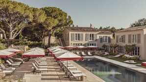 Zona junto a la piscina con tumbonas y sombrillas, una piscina y un edificio con tejado de baldosas y ventanas.
