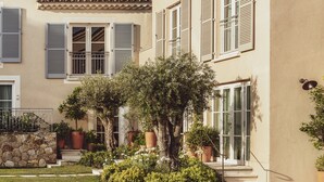 Un edificio con varias ventanas, un muro de piedra y un jardín cuidado con diversas plantas y un árbol.