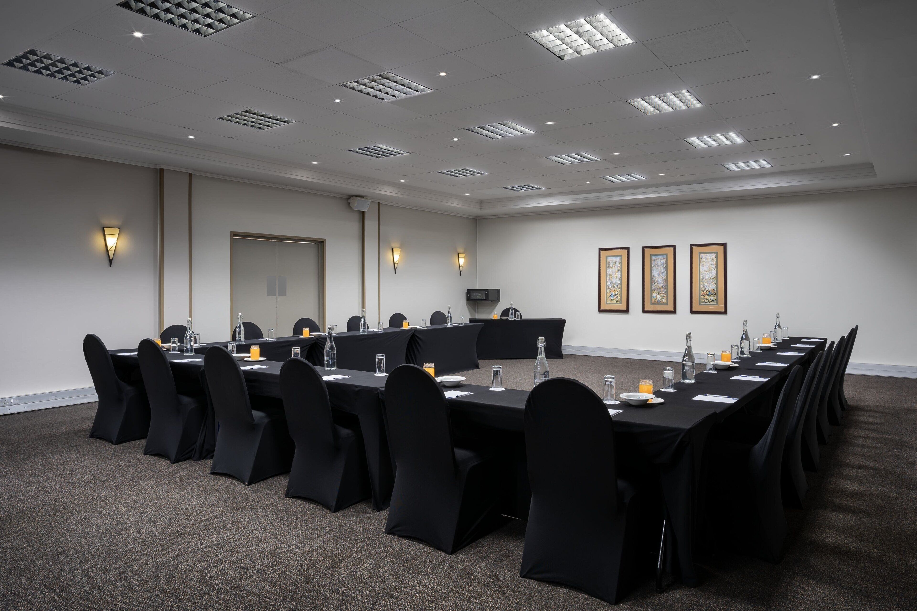 Una sala de conferencias con una larga mesa, sillas negras y piso alfombrado.