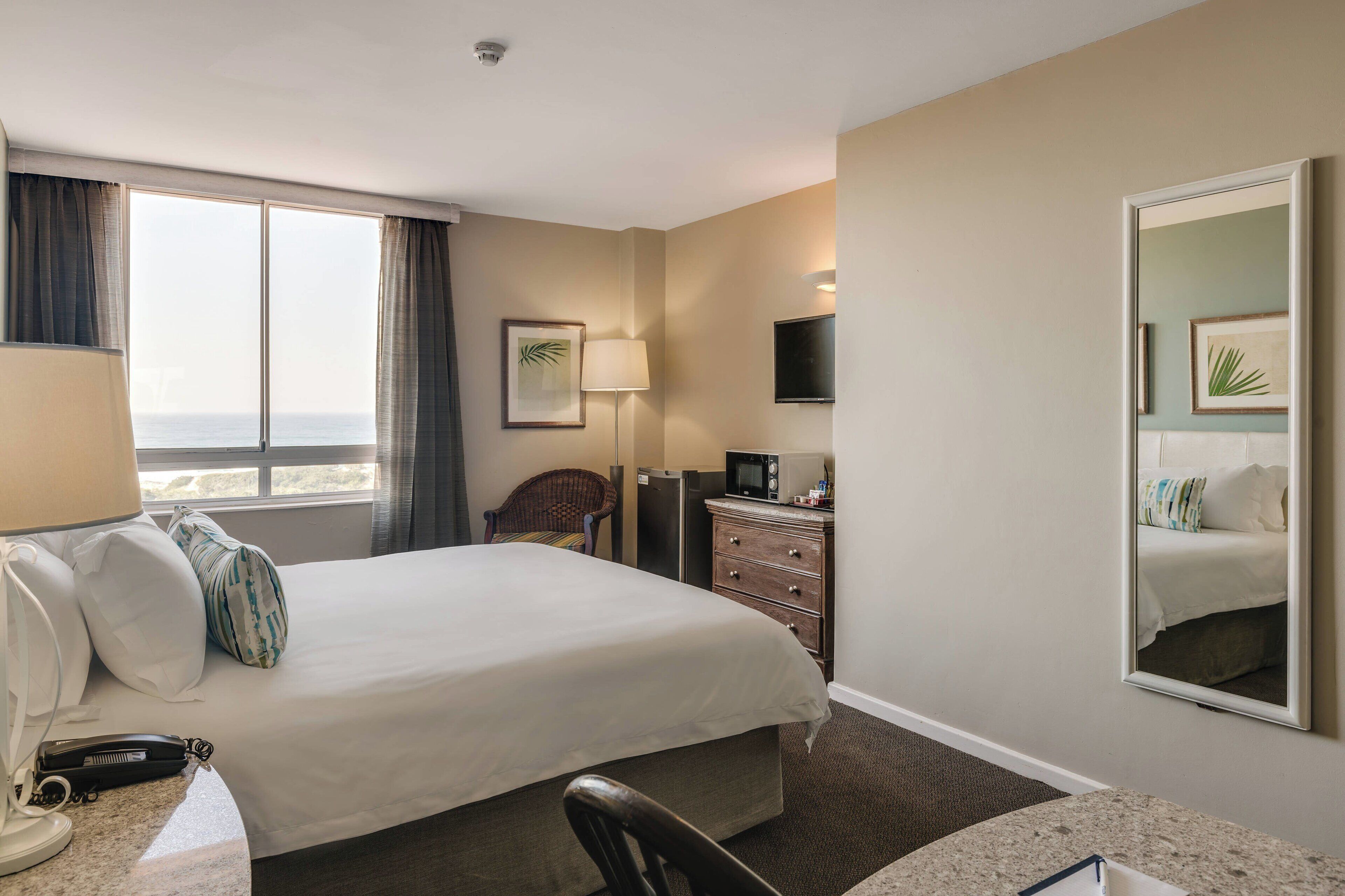 Een hotelkamer met een groot bed, een bureau met lamp, een stoel, een dressoir, een televisie en een raam met gordijnen.