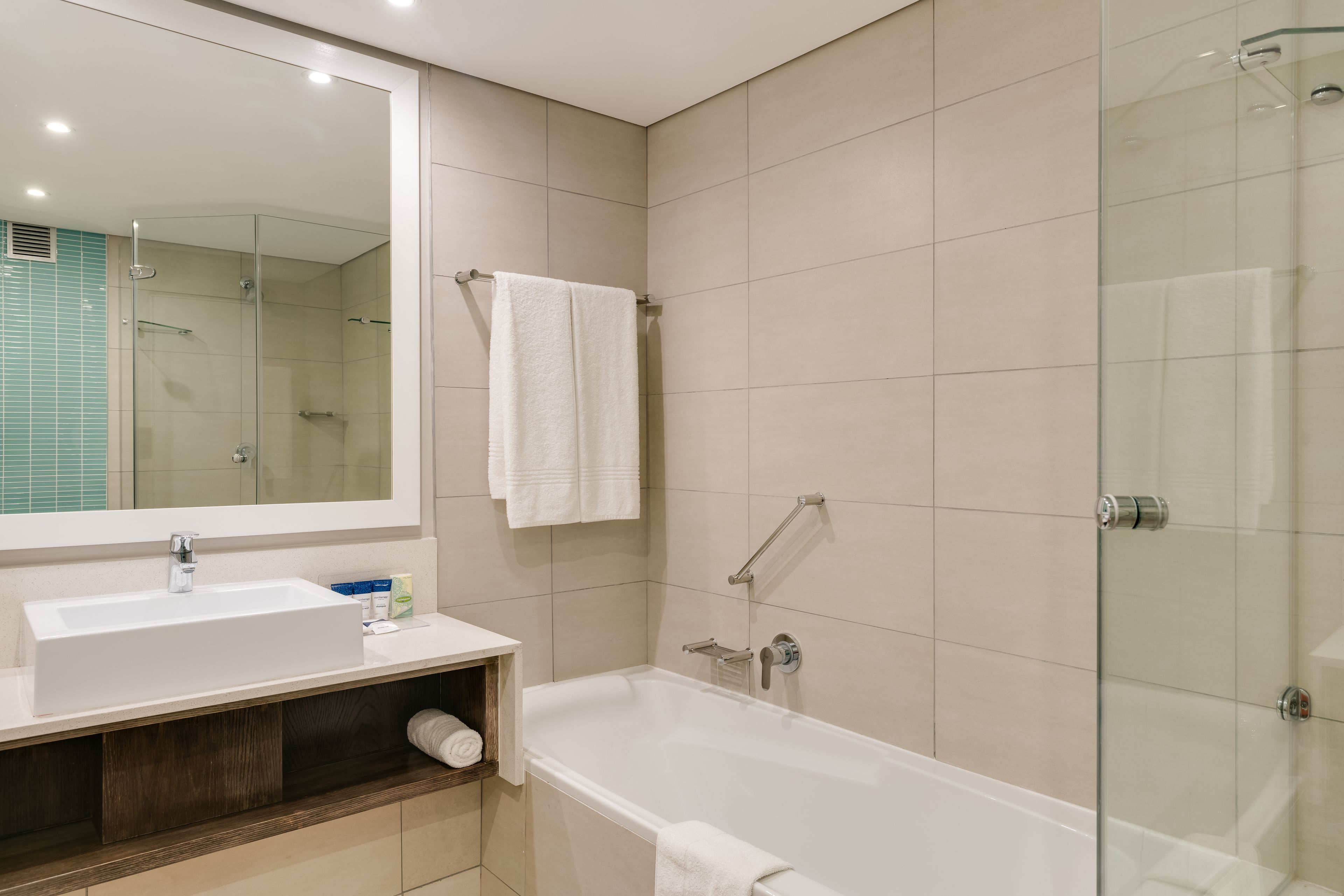 A modern bathroom with a large mirror, a sink, a bathtub, and a glass-enclosed shower.