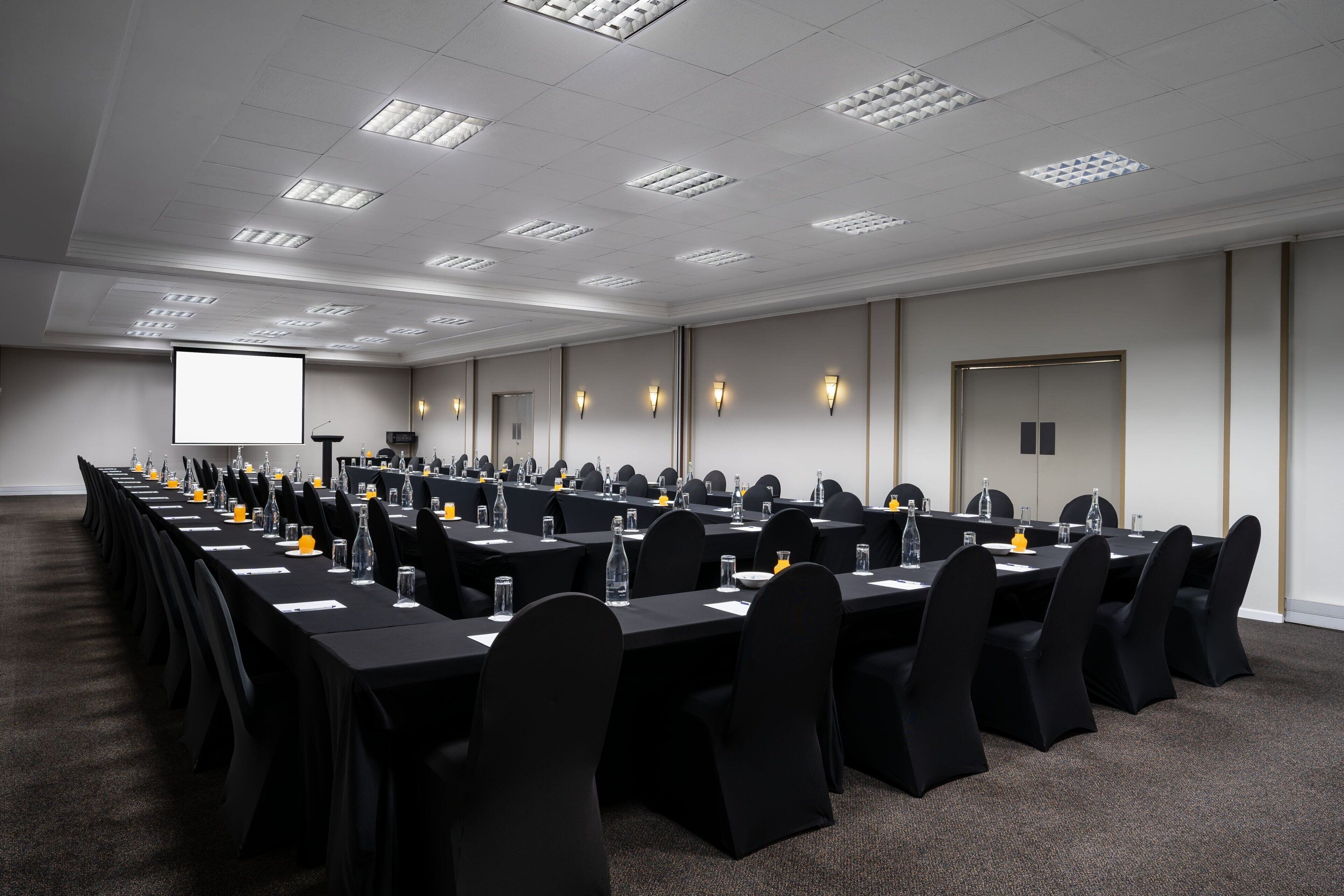 A conference room with long tables, black chairs, and a projector screen.