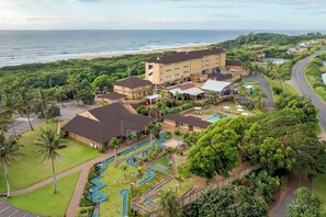 Un resort con zona de piscina, vista a la playa y un edificio grande con varias habitaciones.