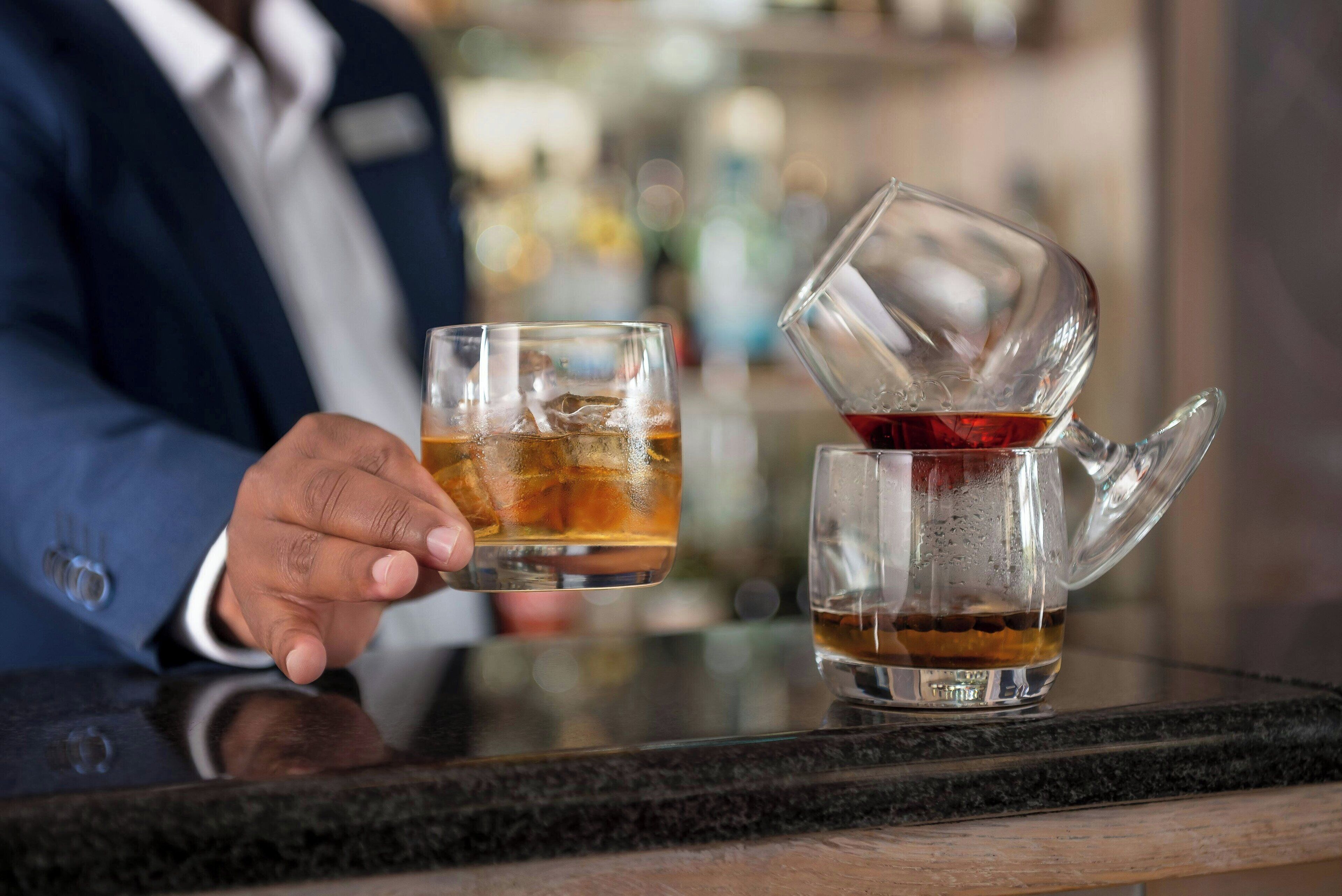A person holding a glass of iced tea, with another glass and a teapot on the counter.