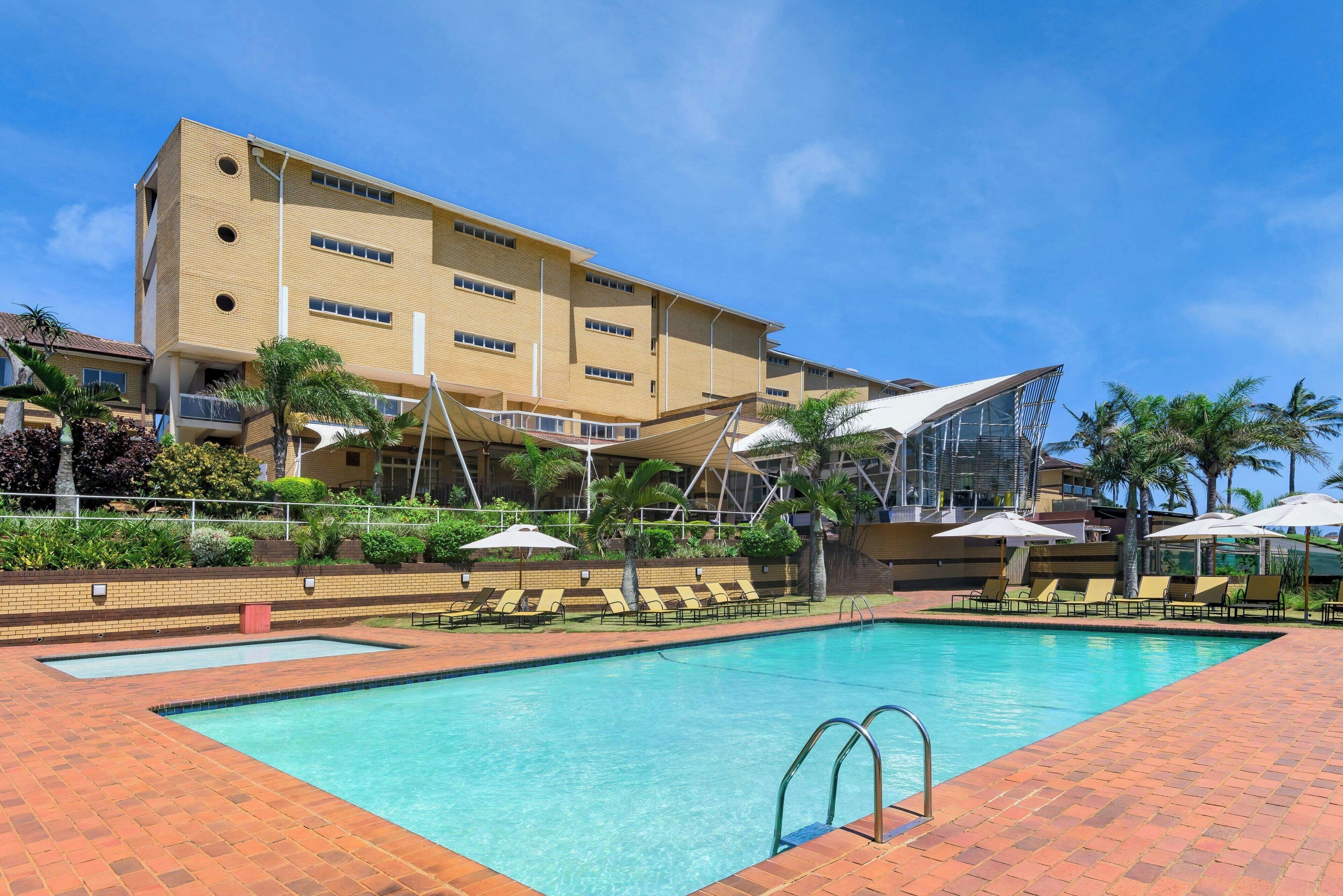 Um hotel com piscina, espreguiçadeiras e palmeiras.