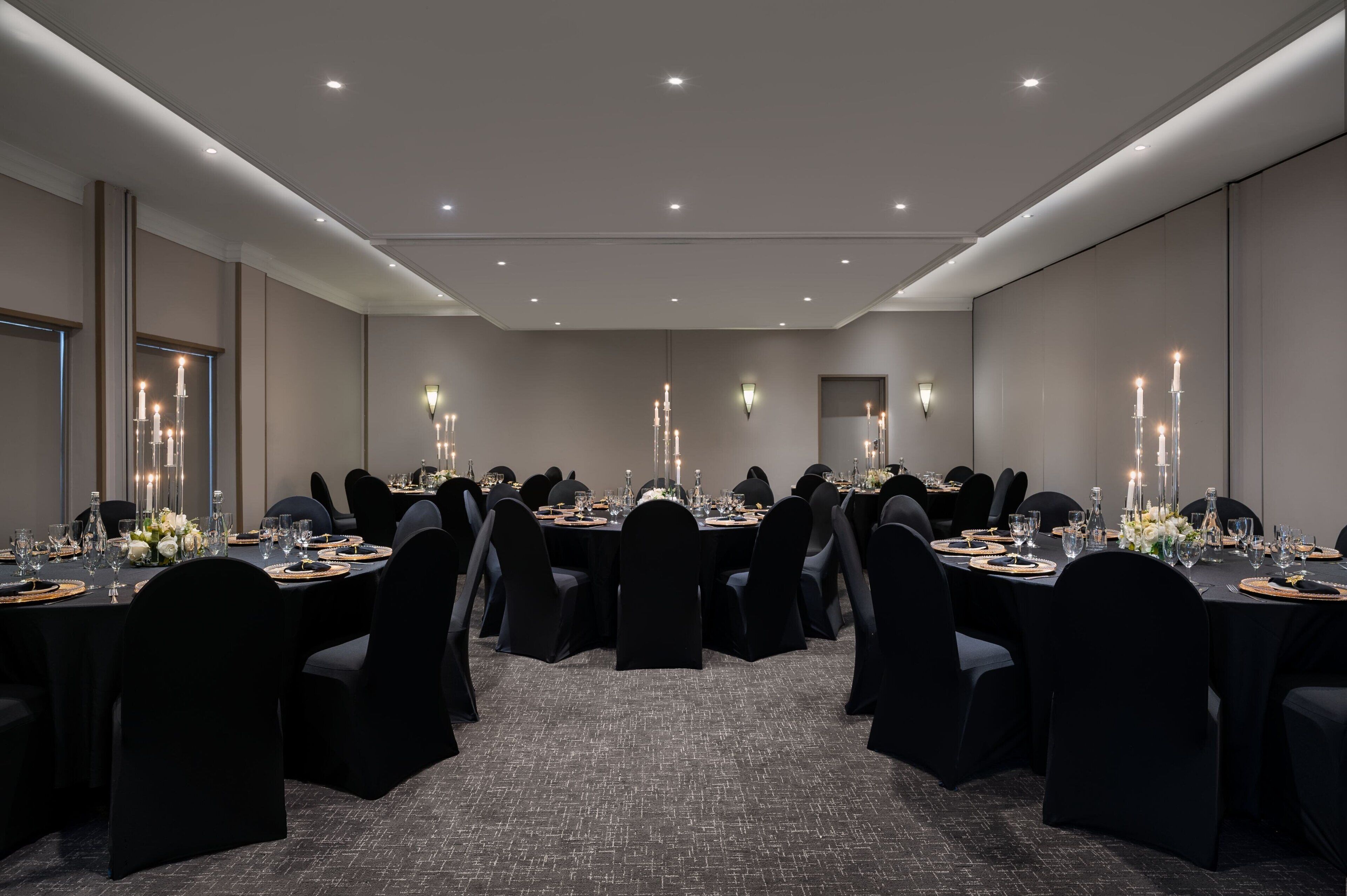 A conference room with round tables, black chairs, and candlelit centerpieces.