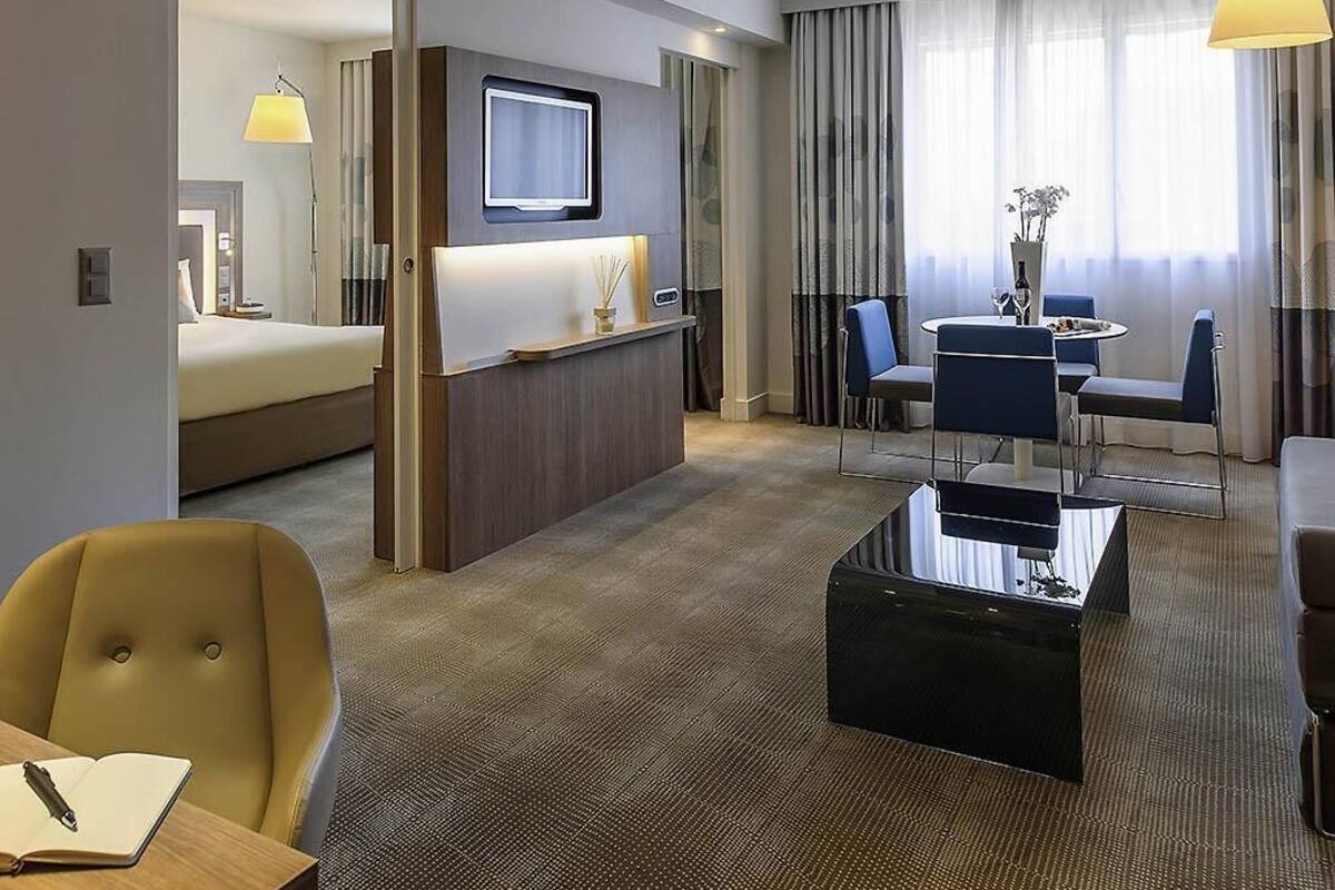 Een hotelkamer met een bed, een bureau met stoel, een zithoek met tafel en stoelen, en een aan de muur bevestigde televisie.
