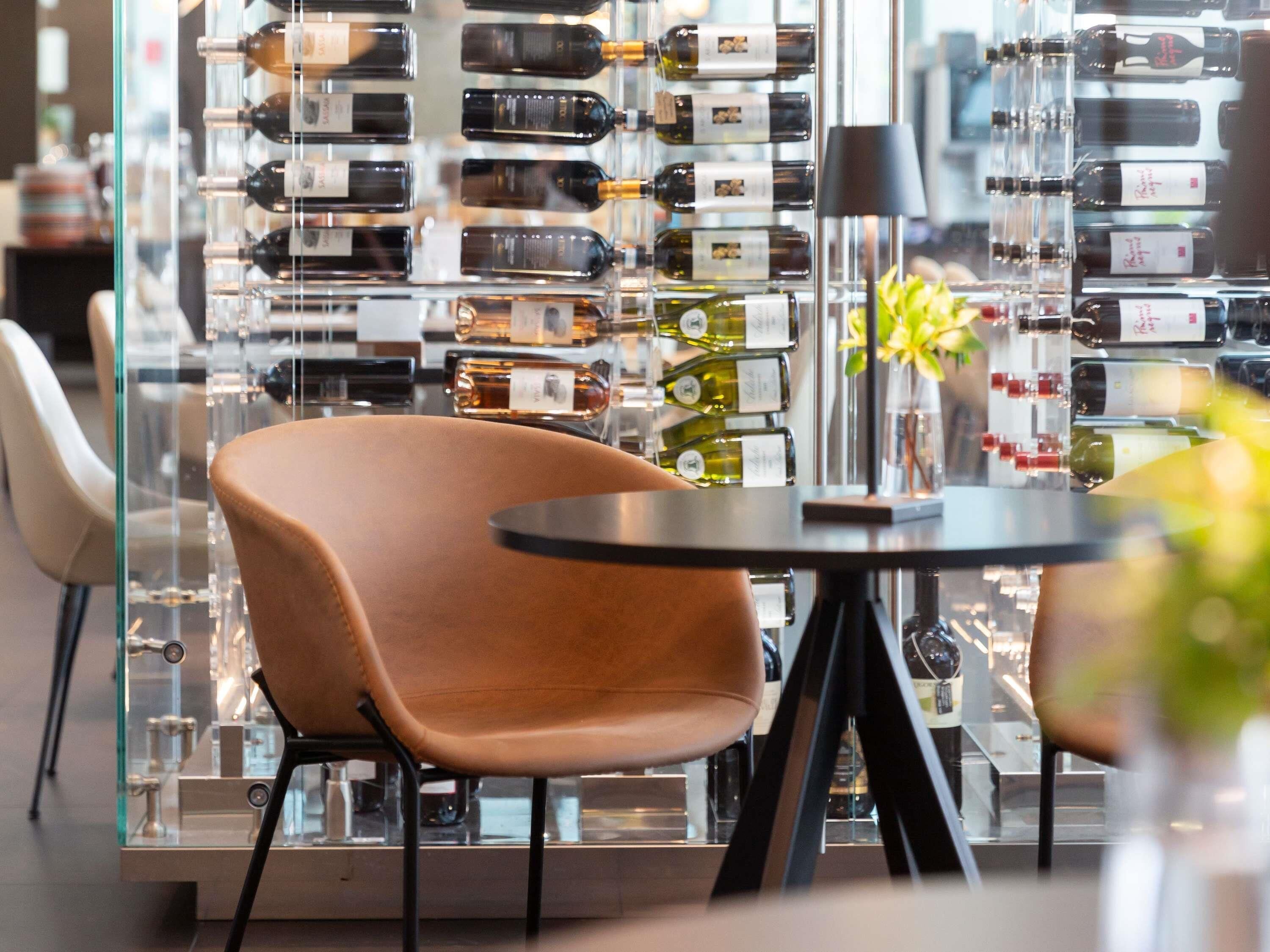 A modern interior with a glass display of wine bottles, a round table, and a brown chair.