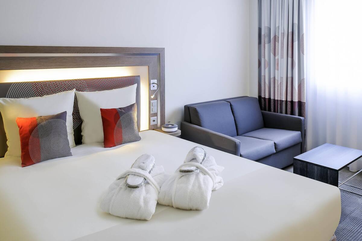 Een hotelkamer met een bed, een grijze bank, een kleine tafel en een nachtkastje met een lamp.