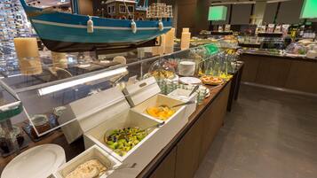 Zona de buffet con diversas opciones de comida, entre ellas frutas, ensaladas y postres.