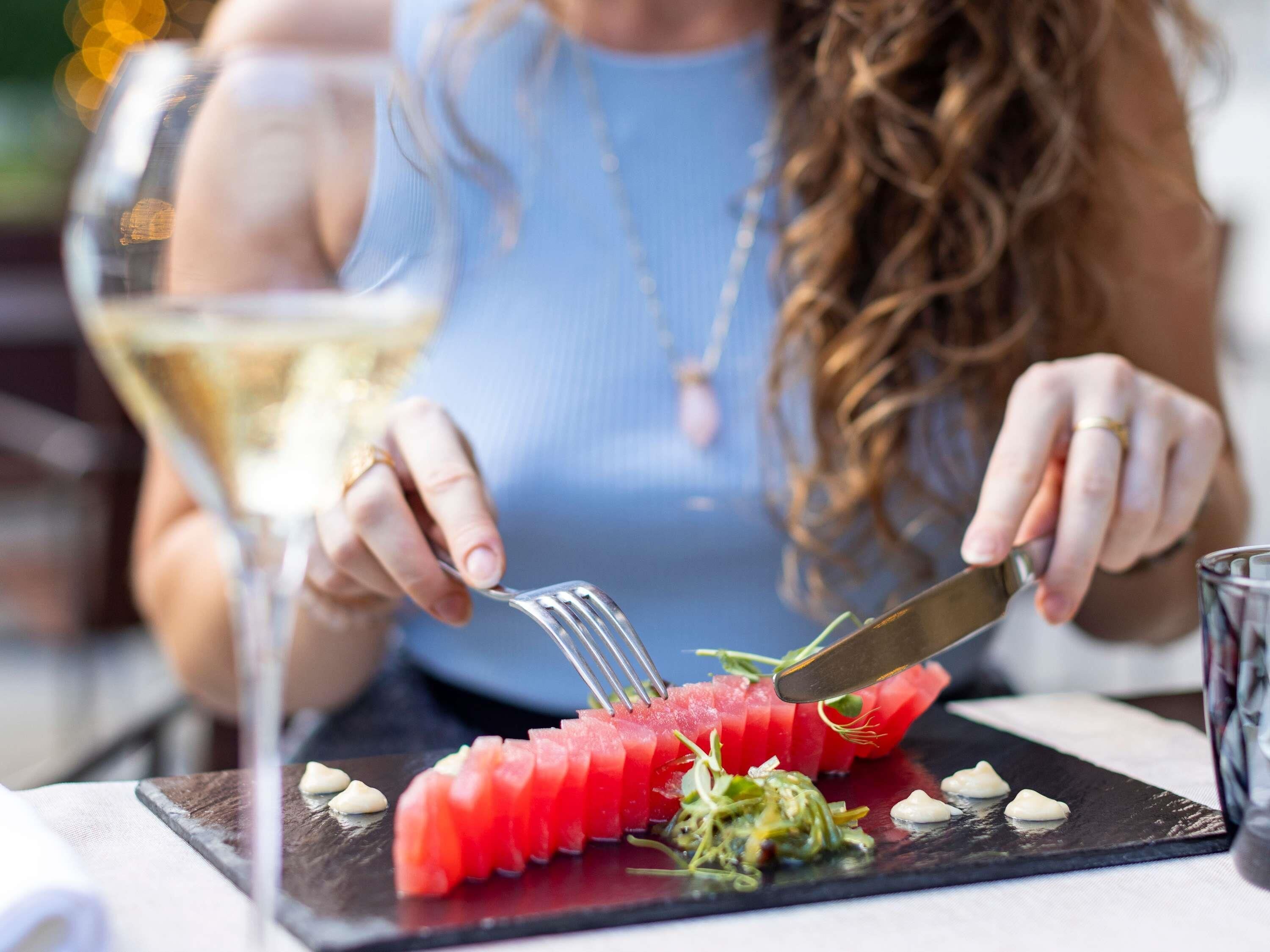 A person dining with a watermelon dish and a glass of white wine.