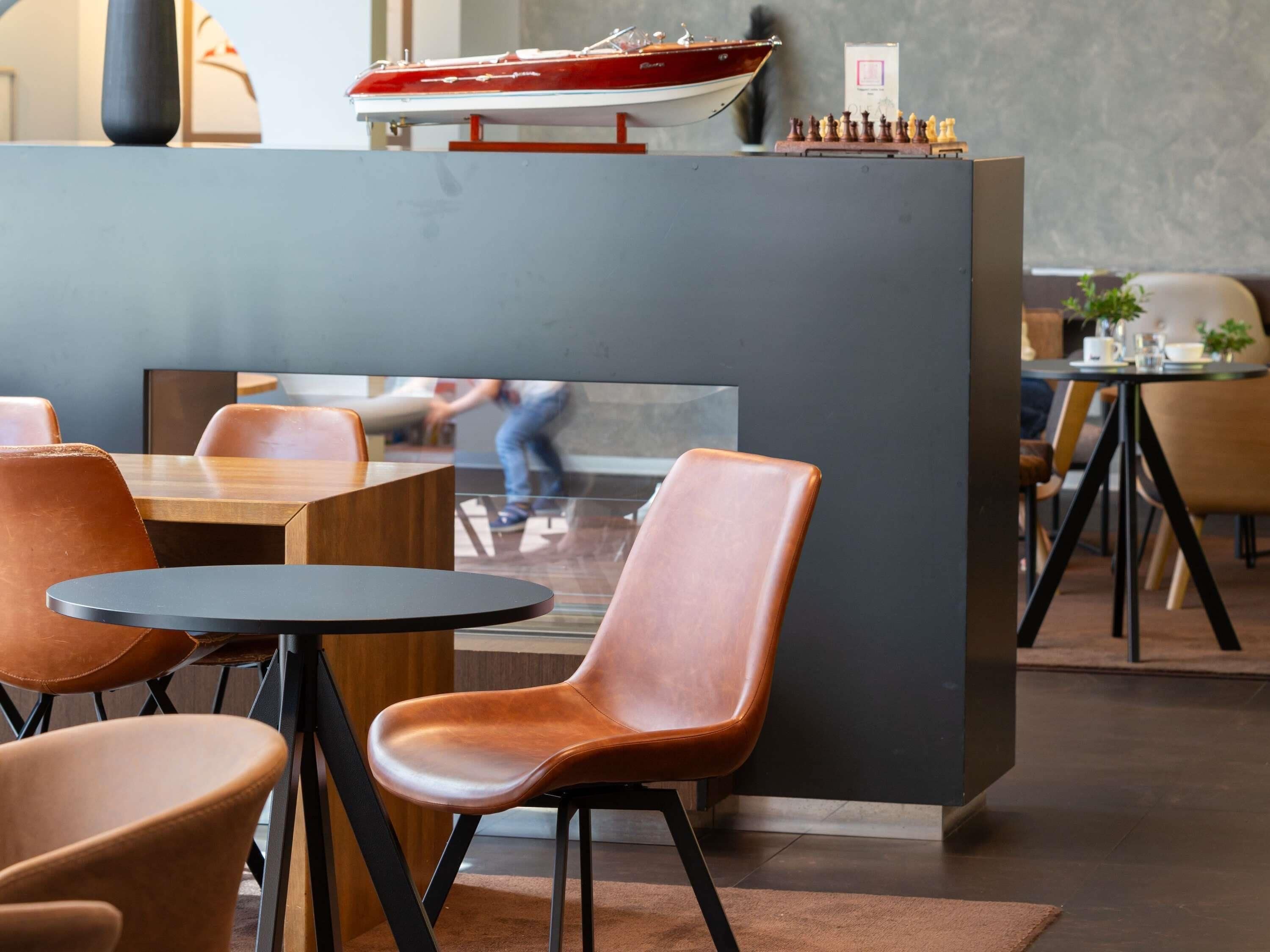 A modern restaurant interior with round tables, leather chairs, and a decorative boat model on a shelf.