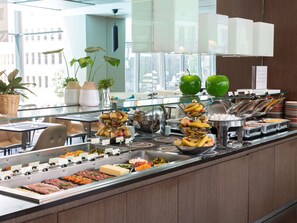 A buffet with various food items, including fruits, meats, and cheeses, in a modern setting with glass partitions and potted plants. - Novotel Lugano Paradiso (Paradiso)
