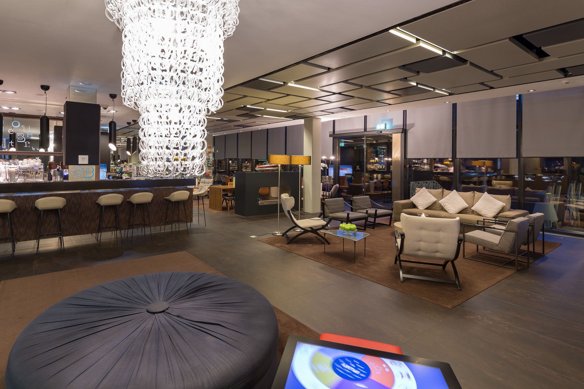 En modern hotellobby med en bardel, sittplatser och en stor kristallkrona.
