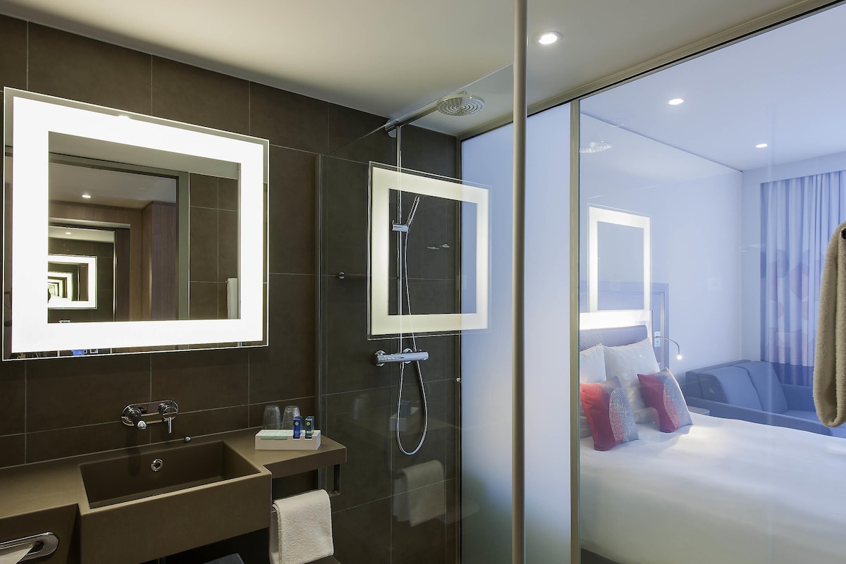 A modern bathroom with a glass shower enclosure, a large mirror, and a vanity with a towel rack.