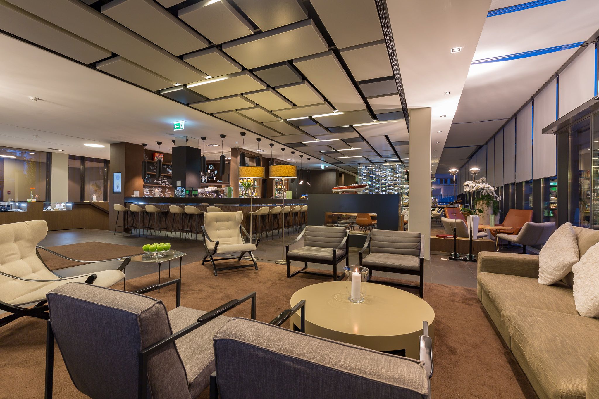 Una hall moderna di un hotel con zone relax, un bar e vista sulla città.