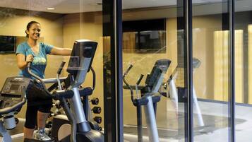 A gym with stationary bikes and a treadmill, glass walls, and a ceiling with recessed lighting.