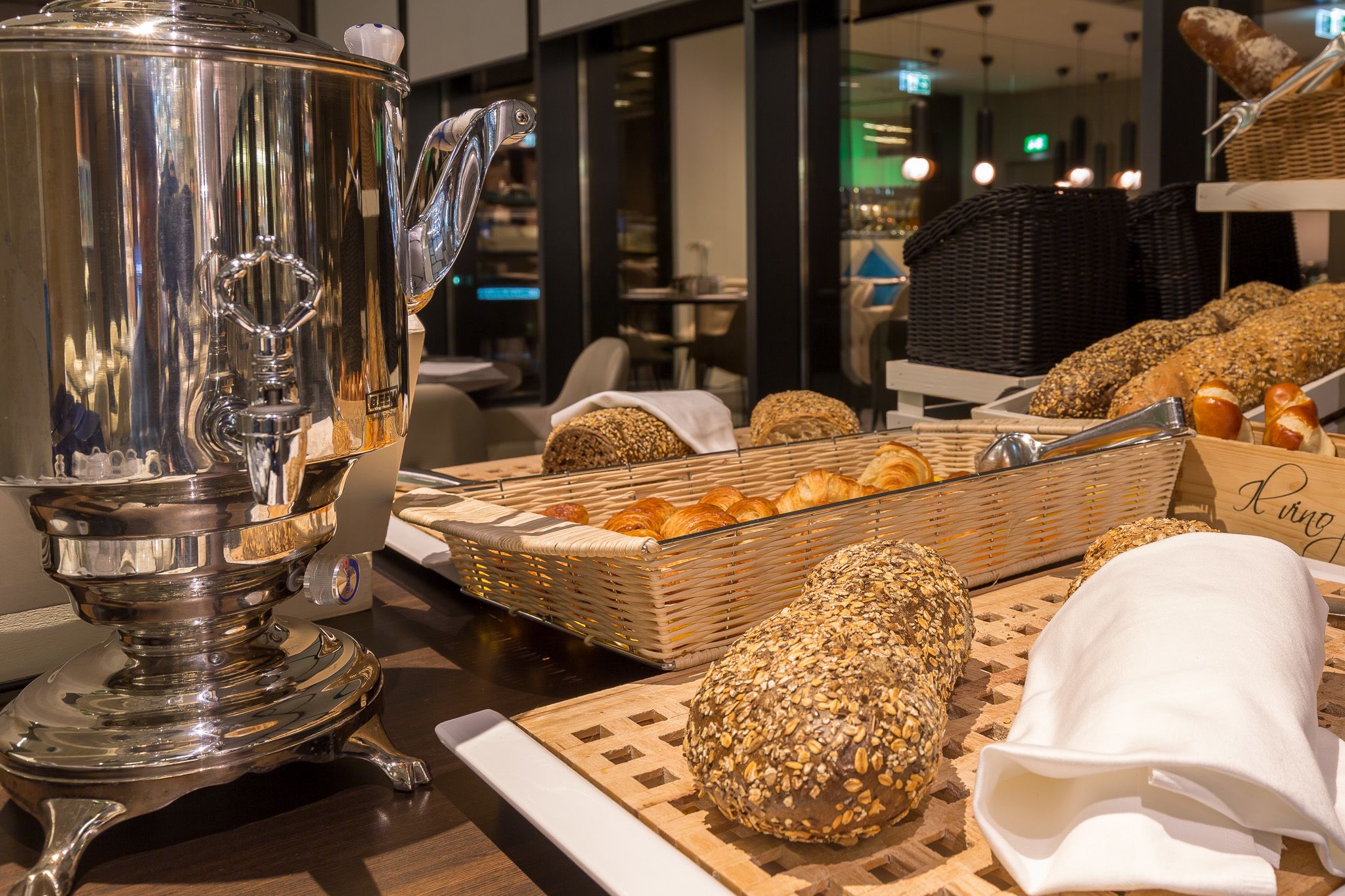 A buffet setup with a silver teapot, various breads, and baskets of pastries.