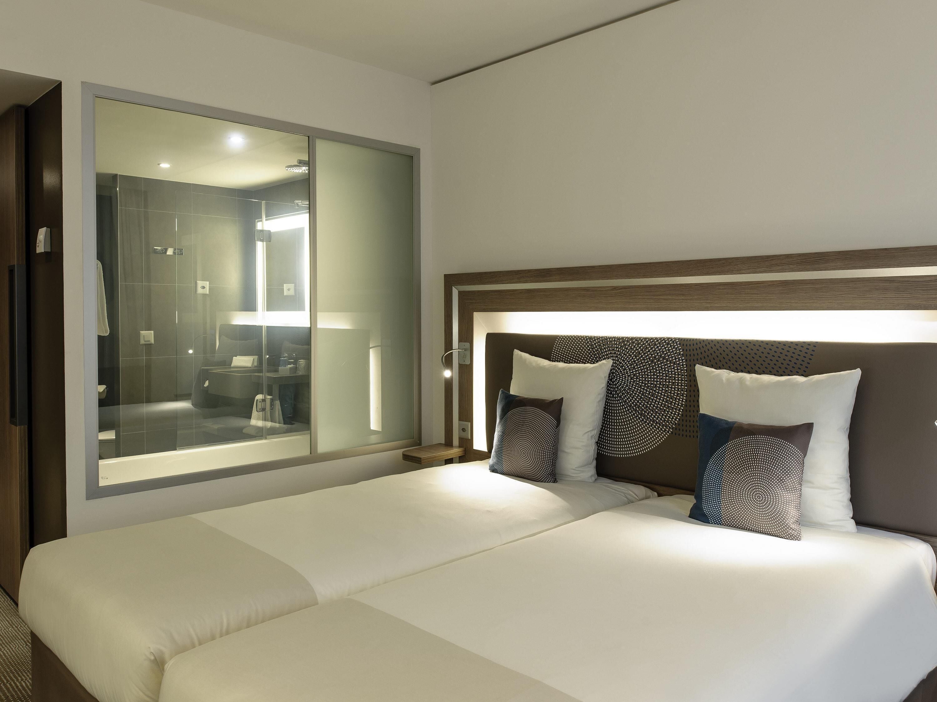 Una habitación de hotel con una cama grande, cabina de ducha de vidrio y tablero de cabecera de madera.