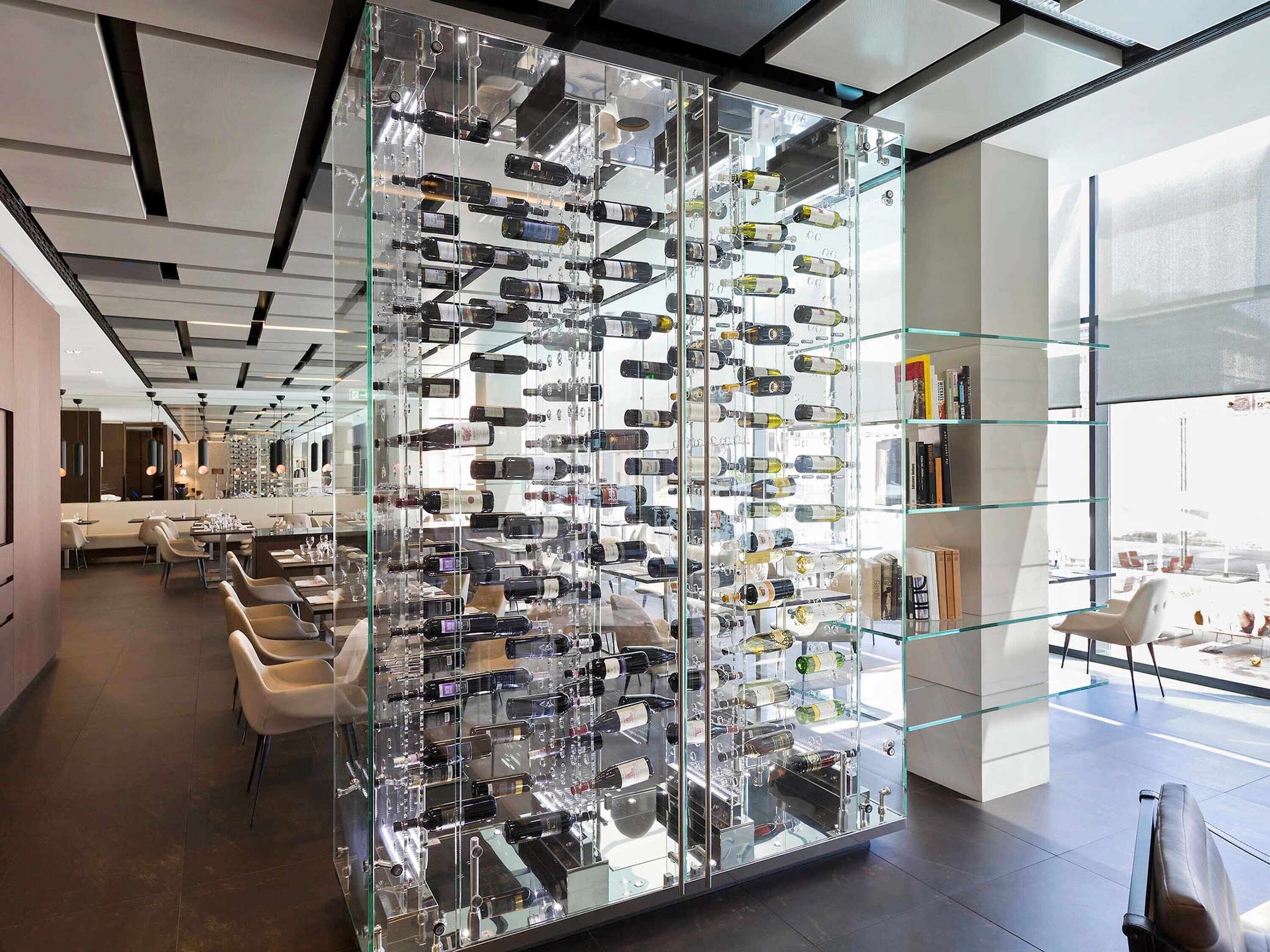 Ein modernes Interieur mit einer großen Glasvitrine voller Weinflaschen, zeitgemäßen Möbeln und Blick durch große Fenster.