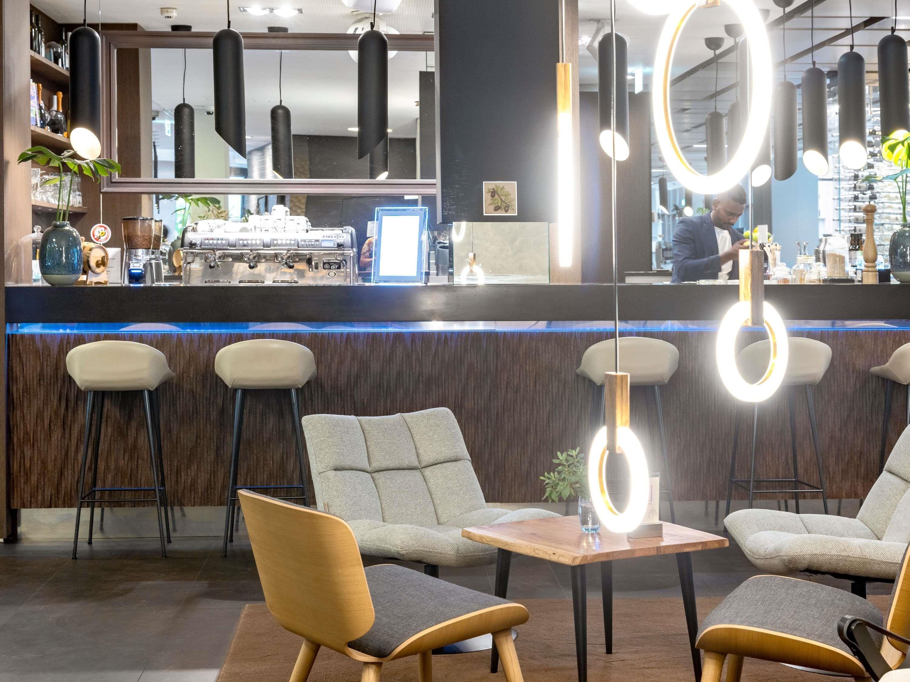 Zona de bar con mostrador, taburetes y asientos, espejo y luces colgantes.