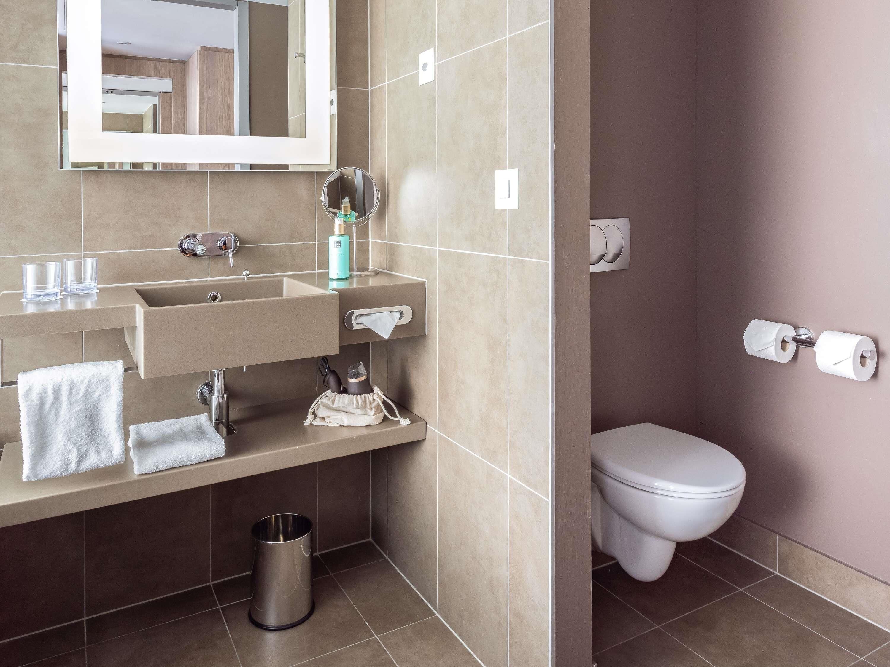 A bathroom with a sink, mirror, towel rack, toilet, and a trash bin.