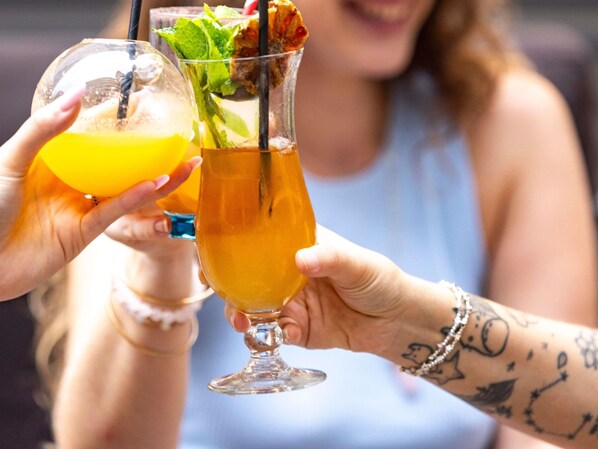 Dos personas sosteniendo bebidas, una con un vaso transparente y otra con un vaso que contiene un líquido amarillo y una pajita.