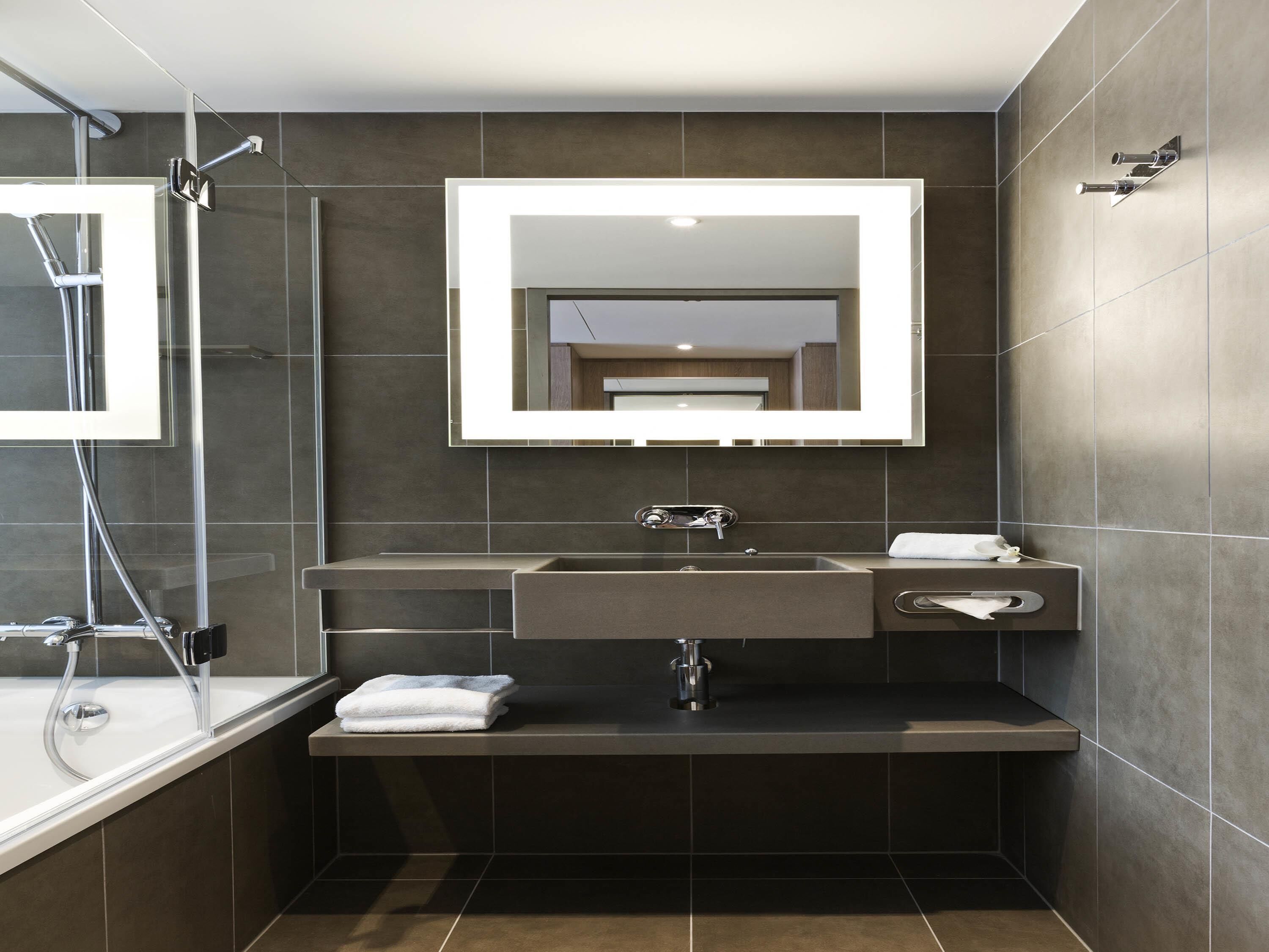 A modern bathroom with a large mirror, a sink, and a shower.