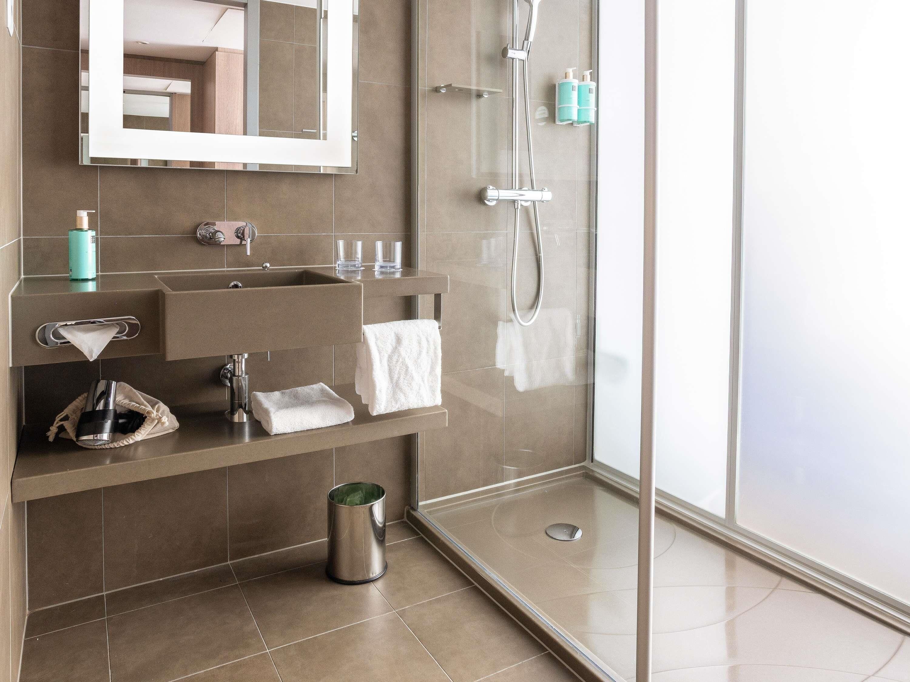 A modern bathroom with a glass shower enclosure, a sink with a mirror above, and toiletries on the wall.