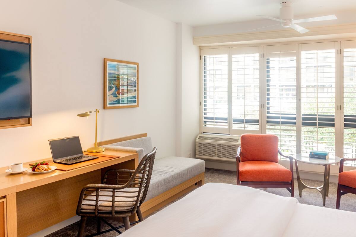 A hotel room with a bed, desk, laptop, chair, and two armchairs.